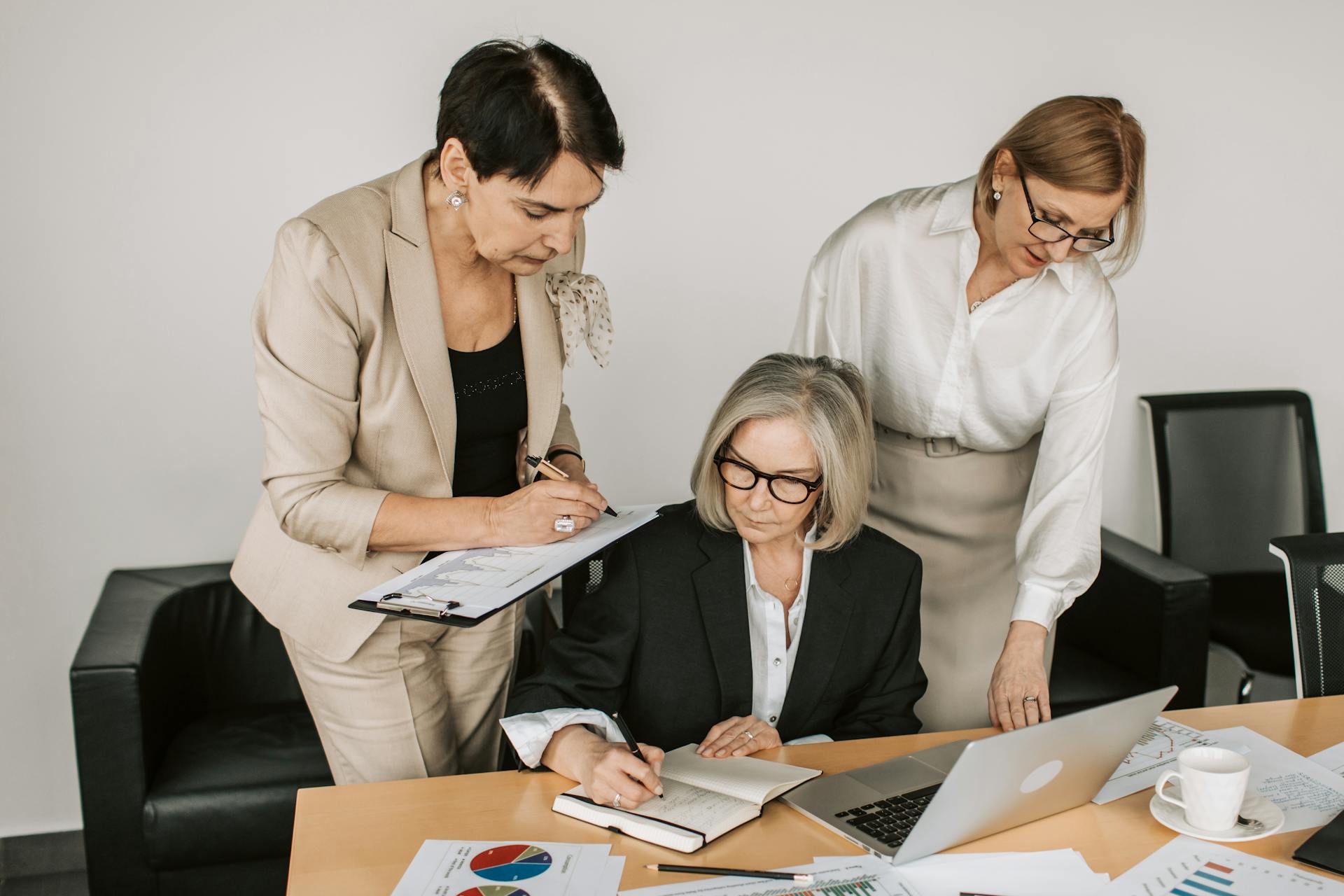 Three professional women collaborating in a business meeting with documents and laptops.