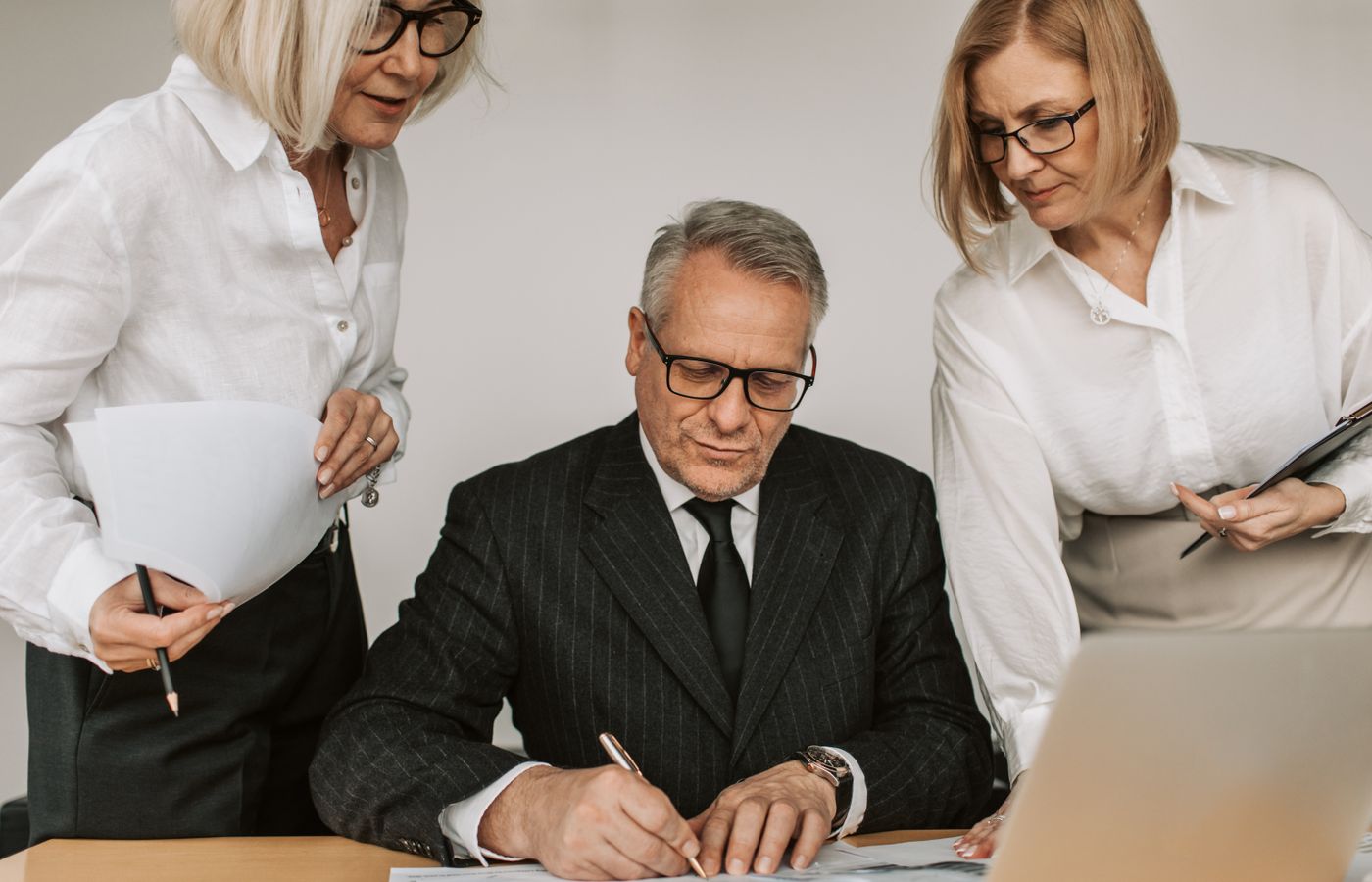 Senior professionals in an office setting reviewing and signing business documents together.
