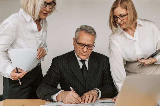 Senior professionals in an office setting reviewing and signing business documents together.