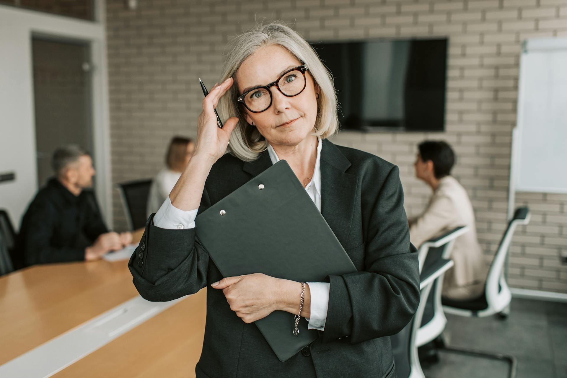 Confident senior businesswoman holding a clipboard in a modern meeting room.