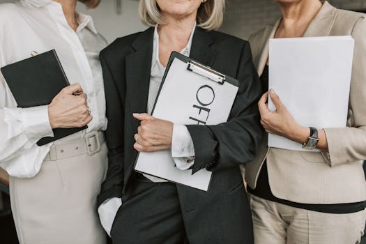 Three businesswomen in attire holding documents and clipboards, conveying professionalism.