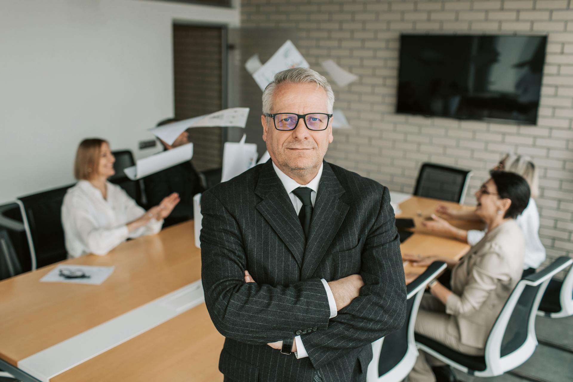 Business executive standing confidently in meeting room with team engaged in discussion behind.