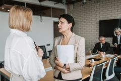 Two businesswomen engage in a conversation during a professional meeting in a modern office.