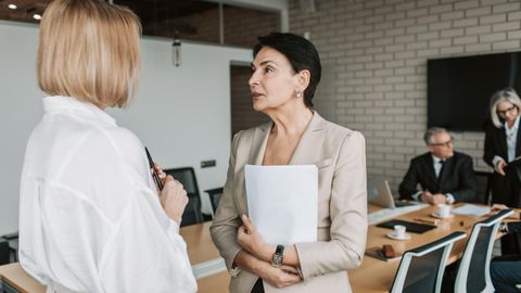 Two businesswomen engage in a conversation during a professional meeting in a modern office.