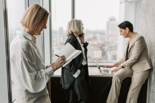 Free Three women collaborating in a modern office with city skyline background. Stock Photo