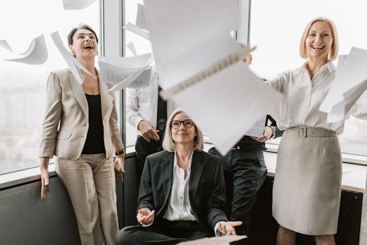 A joyful group of business colleagues celebrates success in a modern office setting.