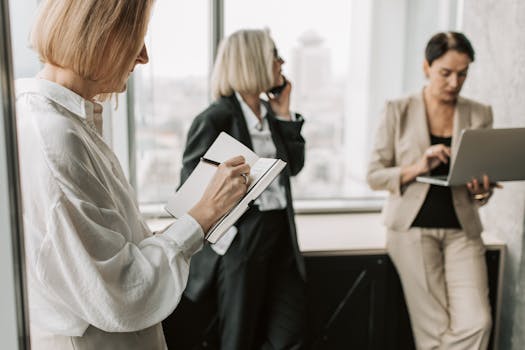 Businesswomen discussing and working in a modern office setting, using a laptop and notebook.
