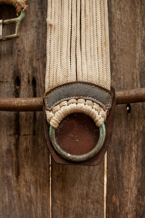 Dirty old belt made of linen ropes with corroded metal ring hanging on timber fence