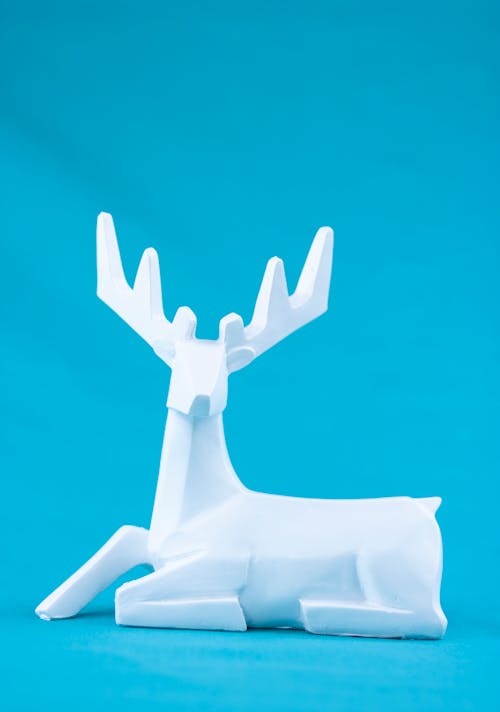 Minimalist style white plaster figurine of lying deer placed against bright blue background