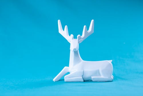 Minimalist style geometric deer statuette made of white plaster placed against vivid blue background
