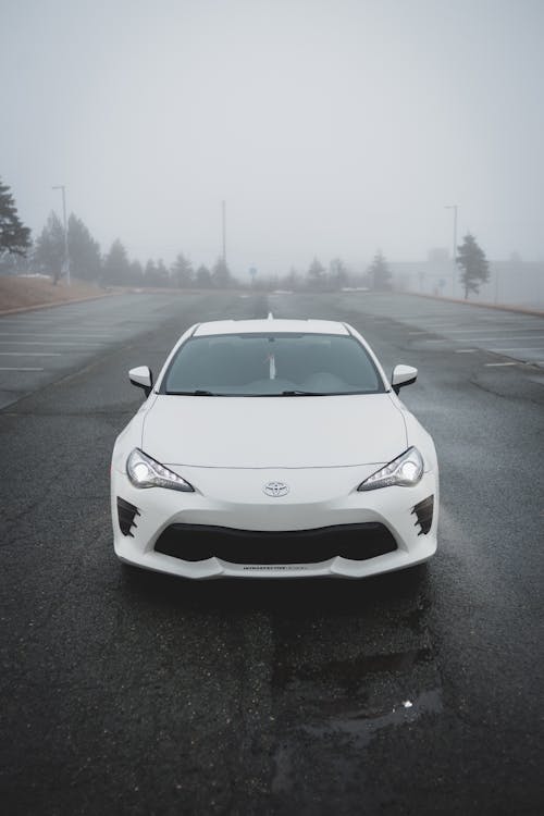 Shiny modern white automobile standing on asphalt roadside with shining headlights and running lights without license plates in rural district in dusk