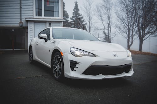 Modern luxury white sport automobile standing near gray house in suburb near wood