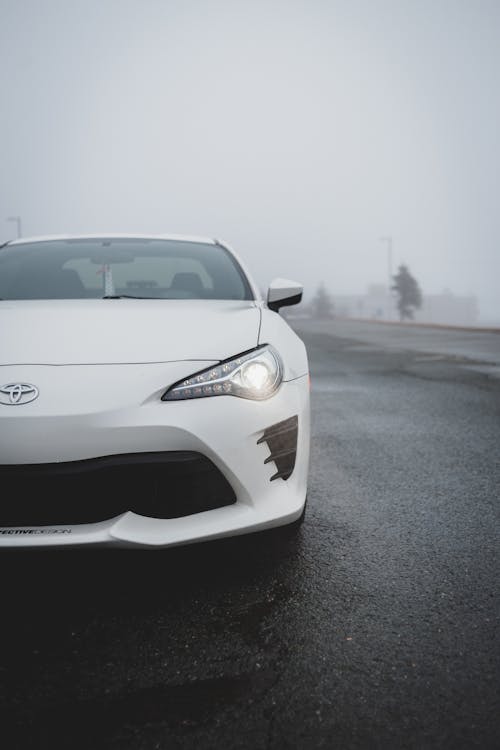 Contemporary sports car with glowing headlights parked on asphalt road in foggy day