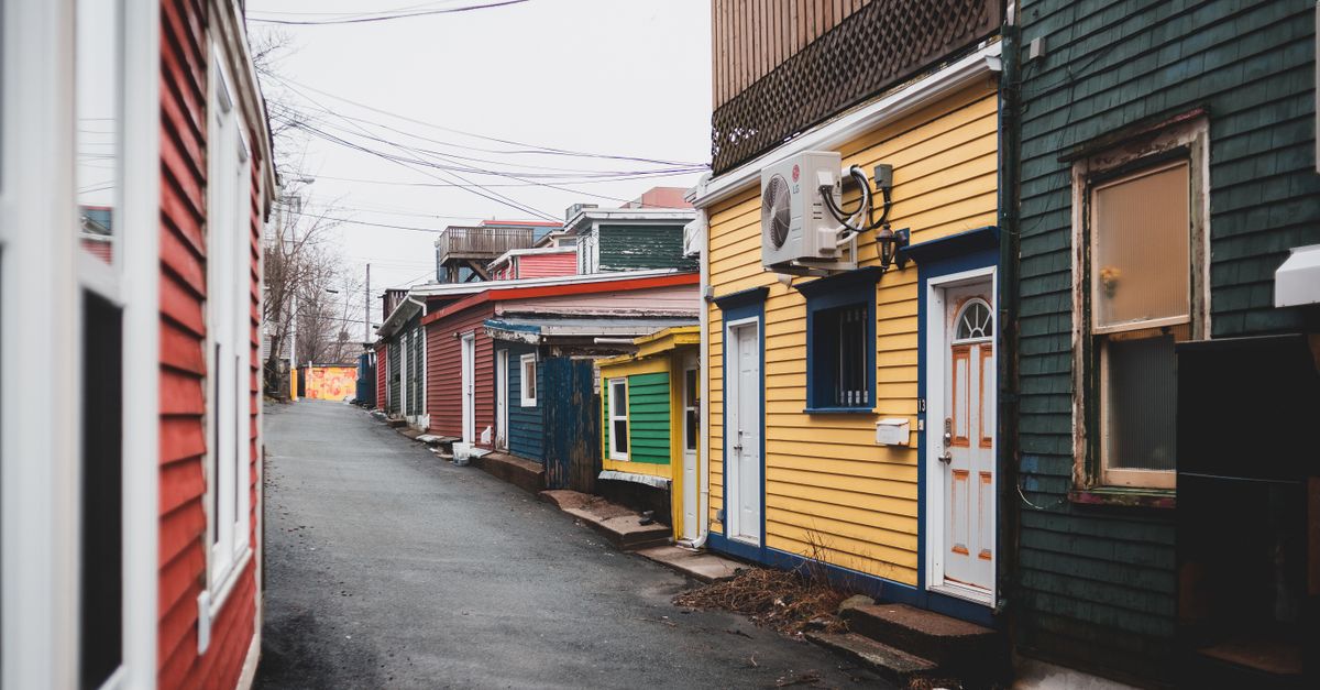 Asphalt way between colorful shabby houses with doors located on street in district of town with power lines against cloudless sky