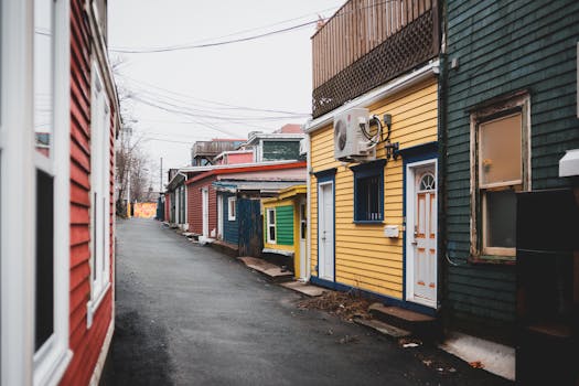 Asphalt way between colorful shabby houses with doors located on street in district of town with power lines against cloudless sky