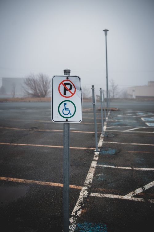 Free White weathered road sign for disabled parking placed on empty parking lot with marking lines on street in misty weather Stock Photo
