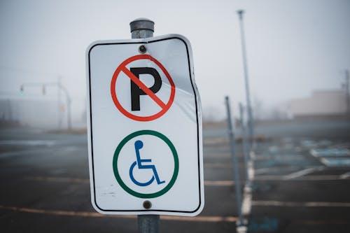 White disabled parking sign on post located on empty asphalt parking lot with marking line on street in foggy weather