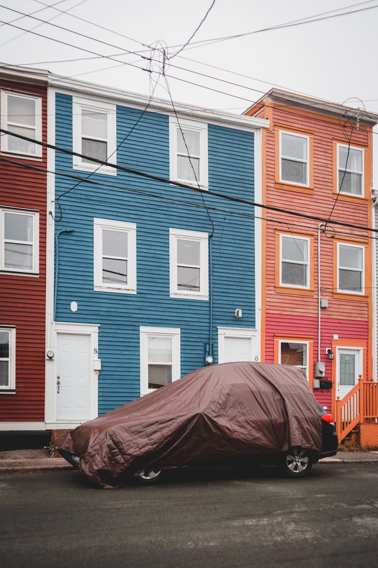 Car Covered With Textile On Road Near Buildings