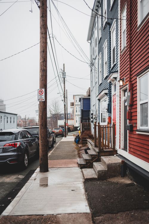 Free Straight sidewalk between colorful residential house with stone steps and roadside with cars on street with power lines in town Stock Photo