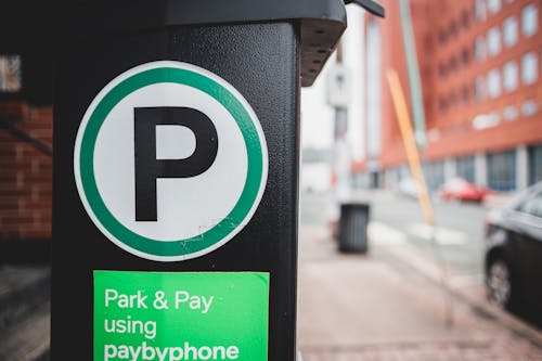 Green sticker for paid parking by phone on black parking meter located on sidewalk near road with cars in city