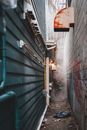 Narrow passage with trash between shabby colorful residential buildings with metal pipes located on street with leafless trees in town