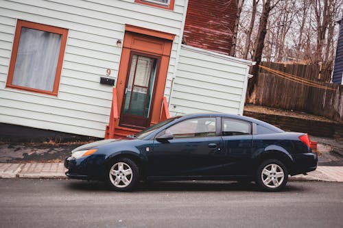 Modern automobile parked on asphalt roadway near aged residential rickety building with window and door located on street of town with leafless trees