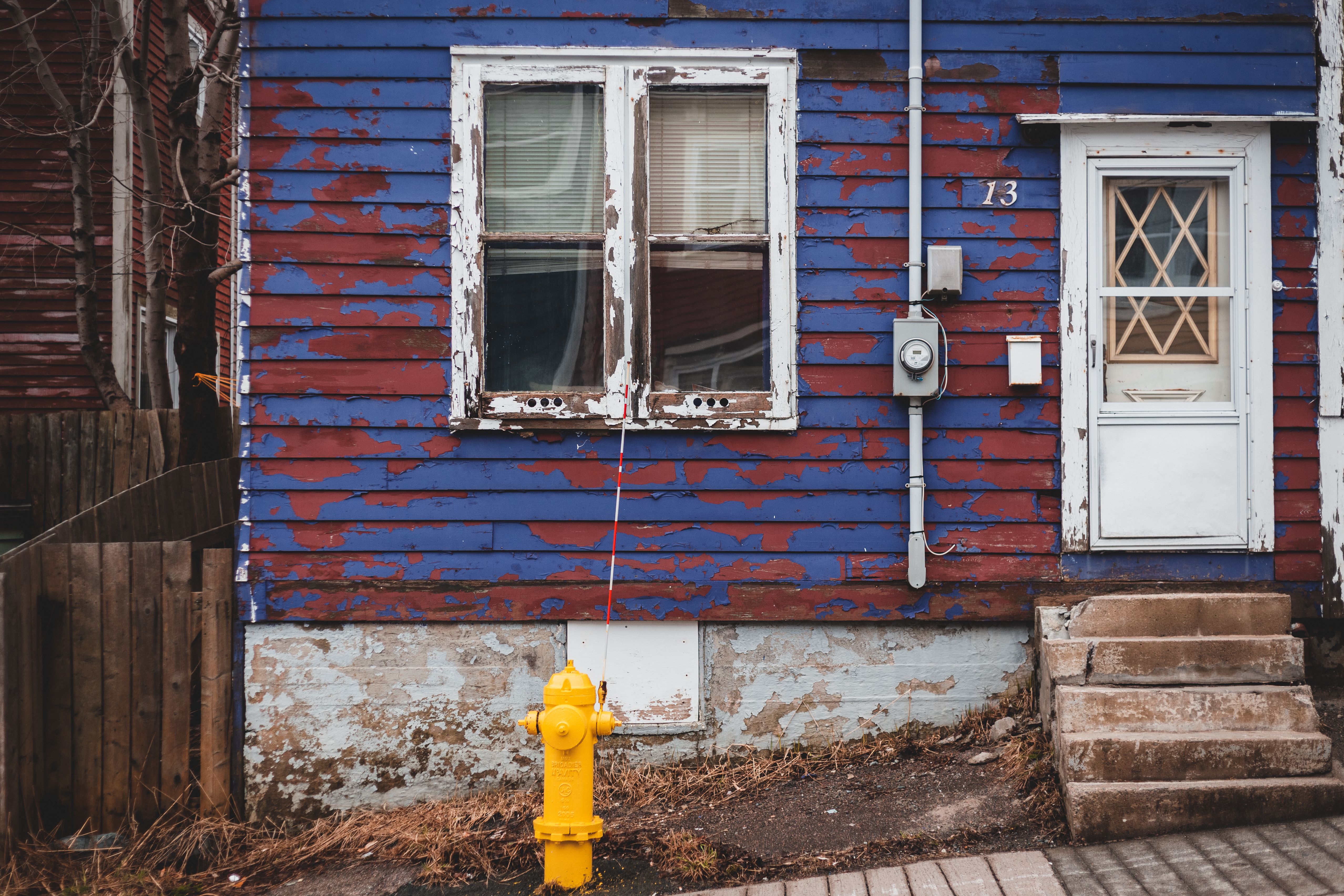 Facade of aged residential house with peeling paint and white door with stairs located near walkway on street of town