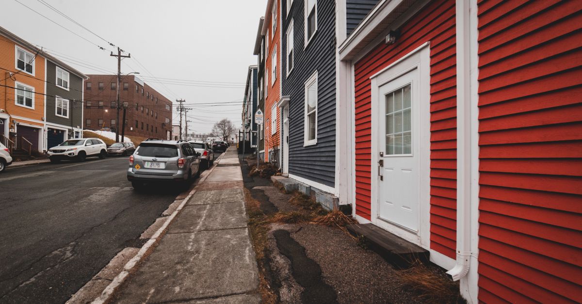 Bright old fashioned residential houses with windows located near asphalt roadway with modern cars on street of town against cloudless sky