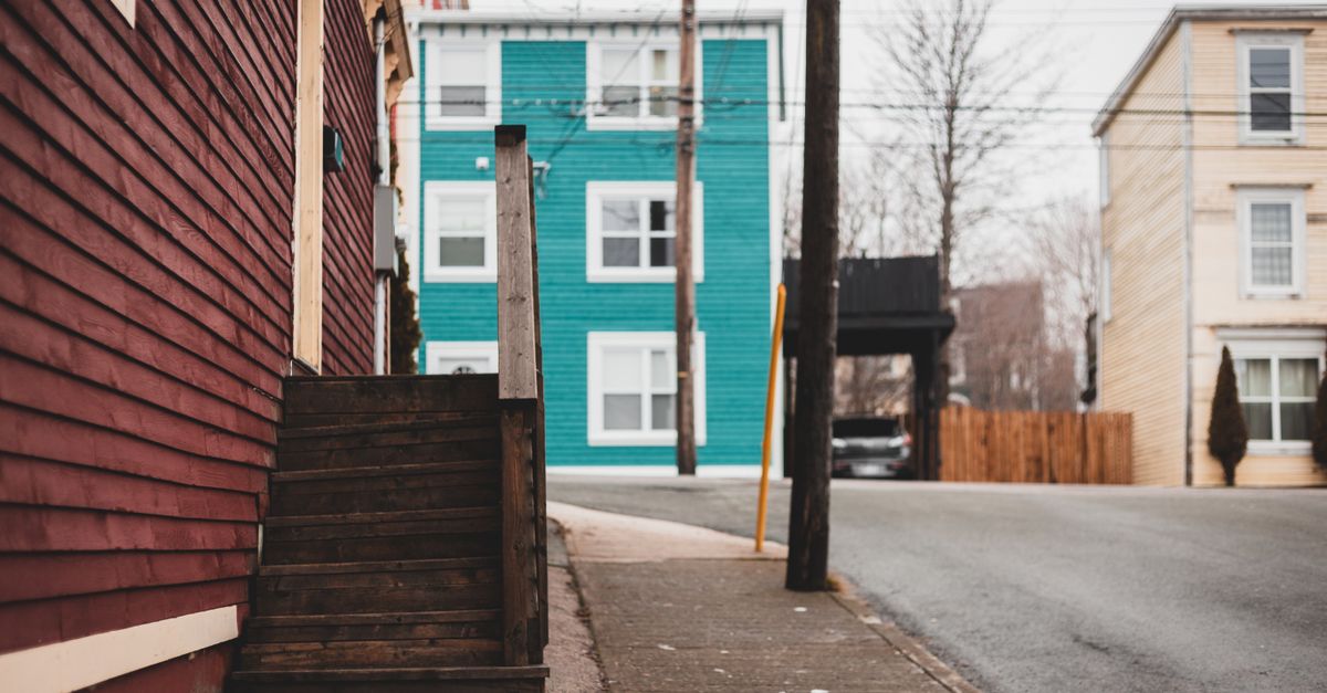 Shabby stairs of residential building located on sidewalk near asphalt road on street with tall pole and houses of town