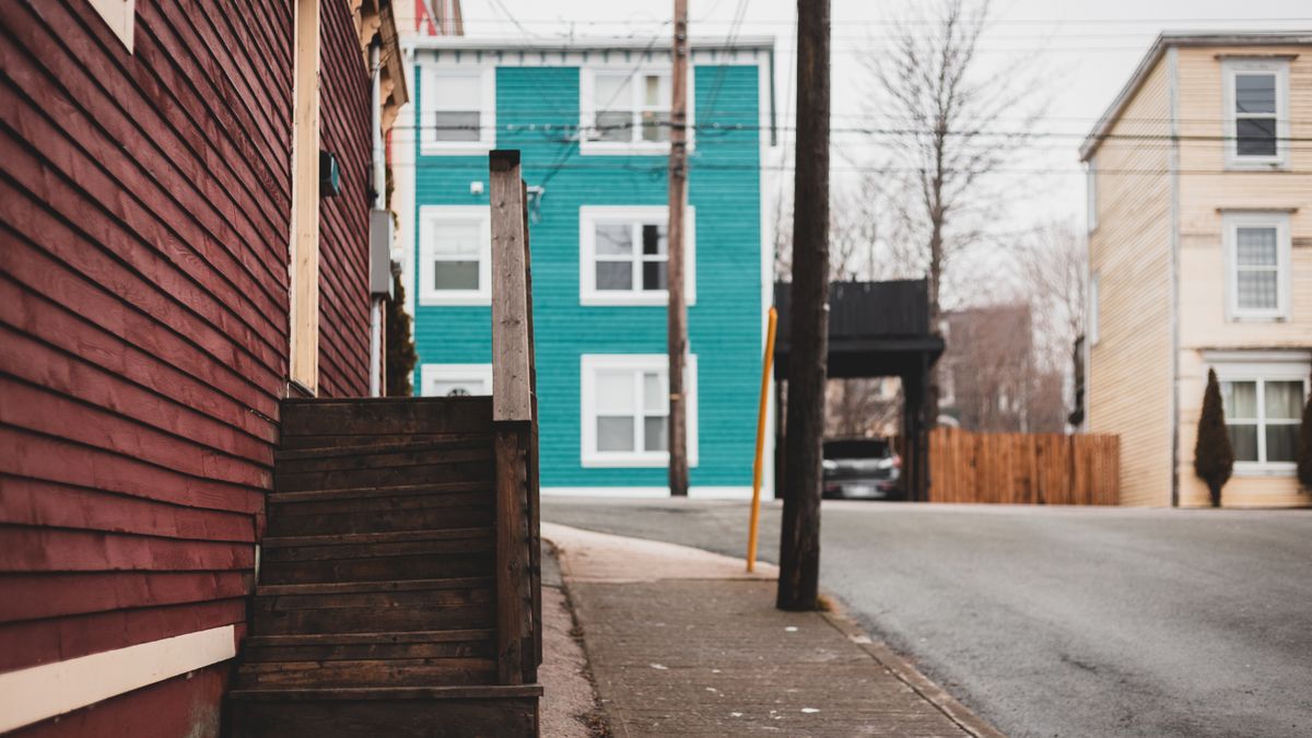 Shabby stairs of residential building located on sidewalk near asphalt road on street with tall pole and houses of town