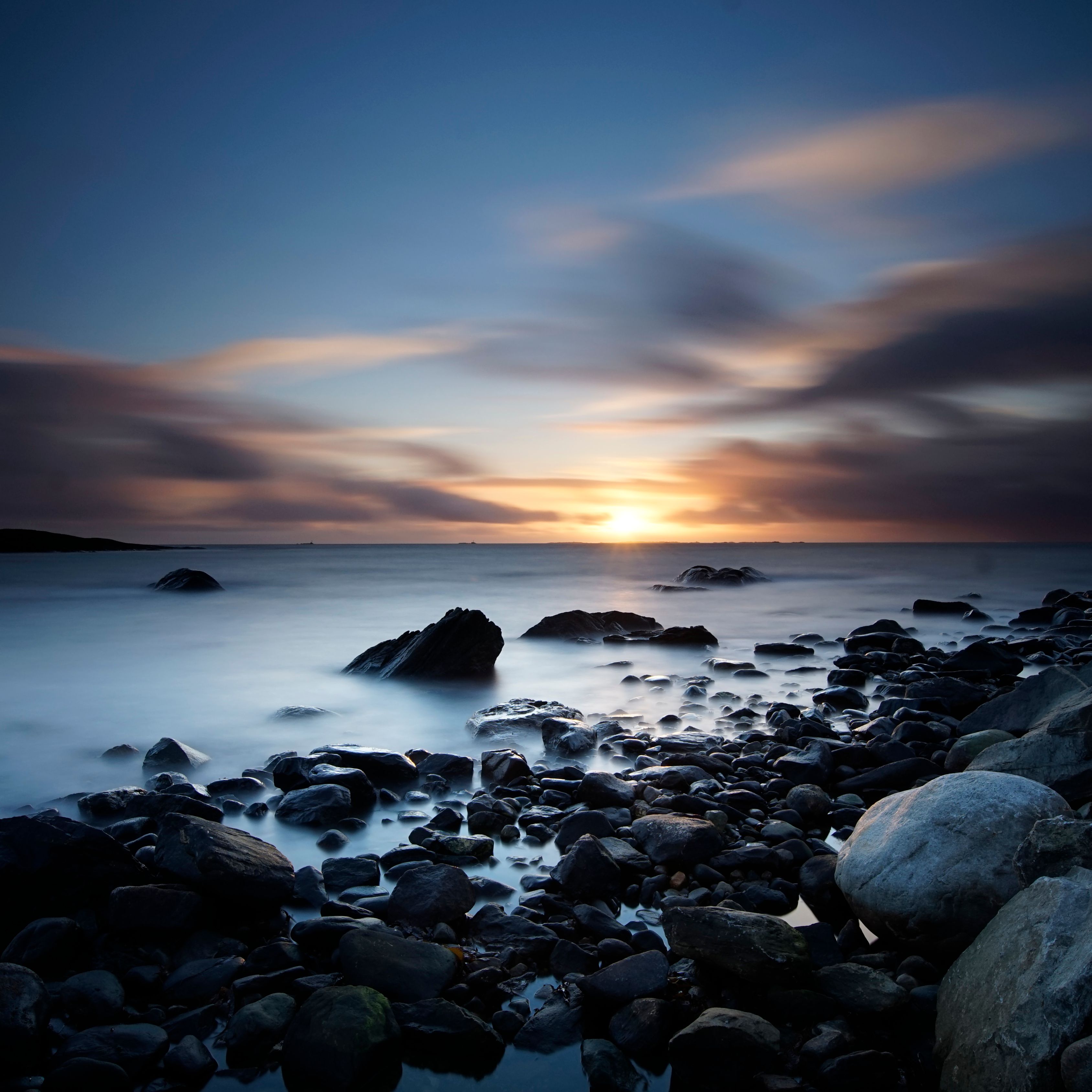 Peaceful long exposure of a rocky beach during sunset with an enchanting seascape view.