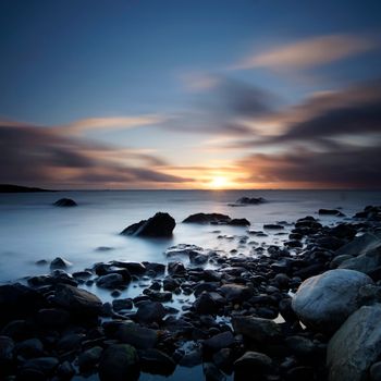 Peaceful long exposure of a rocky beach during sunset with an enchanting seascape view.