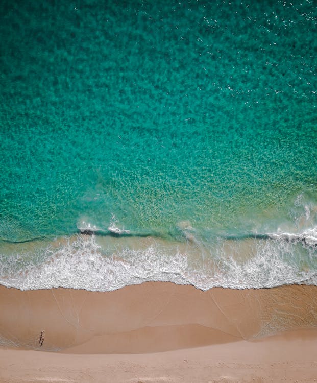 Breathtaking aerial view of bright turquoise ocean with foamy waves washing sandy beach on sunny day in tropical country