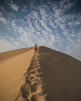 A person walks along the sand dunes under a blue sky in Huacachina, Peru, capturing a sense of adventure and solitude.