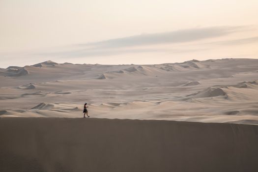 A lone person walking on the expansive sand dunes of Huacachina, Peru.