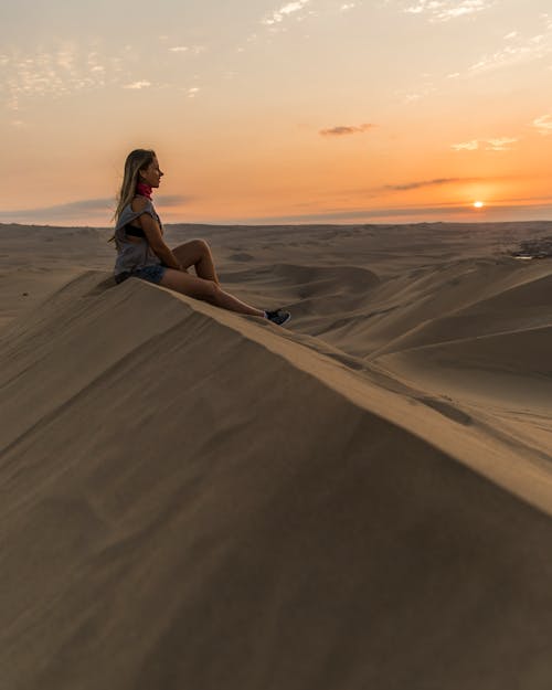 A Woman Sitting on a Sand Dune during Sunset