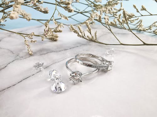 Pair of expensive engagement rings and shiny diamonds placed on marble table near natural plant twigs