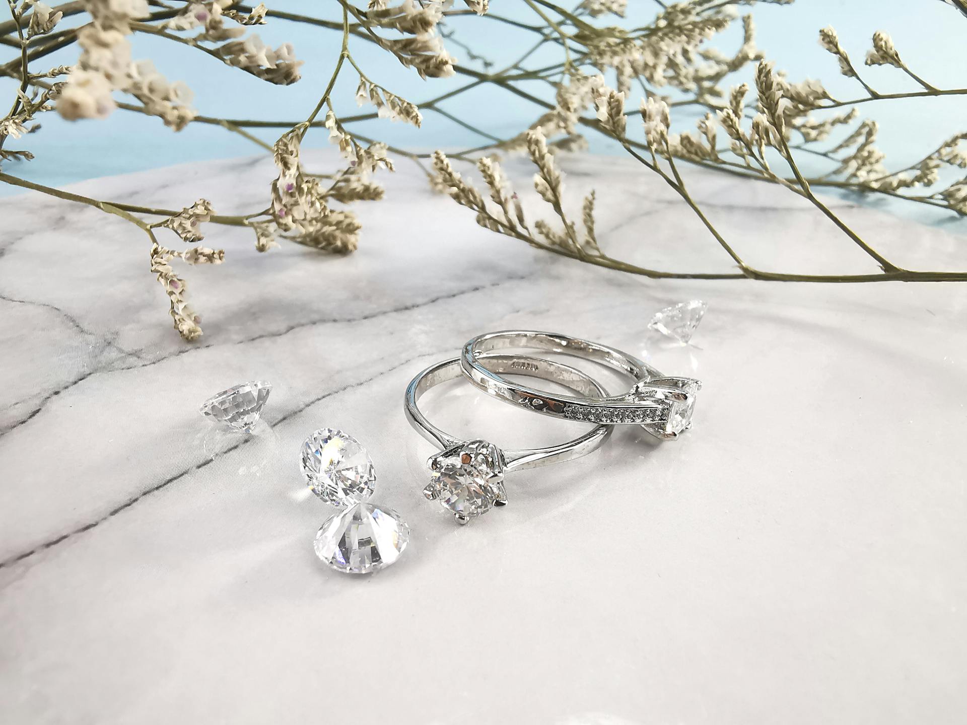 Pair of expensive engagement rings and shiny diamonds placed on marble table near natural plant twigs