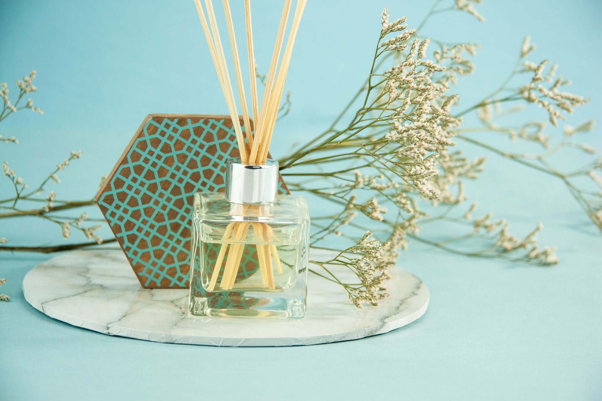 Composition of glass bottle with fluid aroma oil with reed sticks placed near Gypsophila branch and geometric decor on blue background
