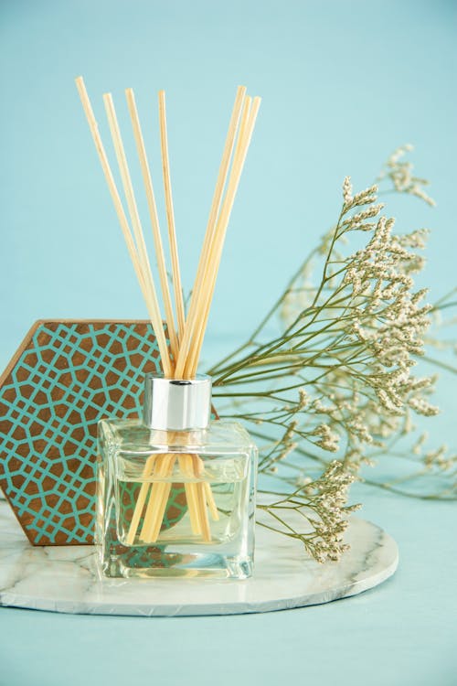 Glass bottle with aroma oil and sticks placed on marble stand near geometric decor and Gypsophila flowers