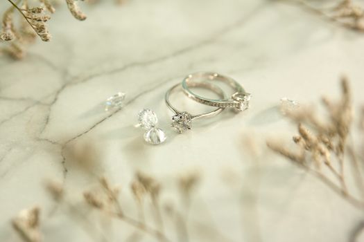 High angle of elegant shiny silver rings and precious diamonds placed near twigs on marble table