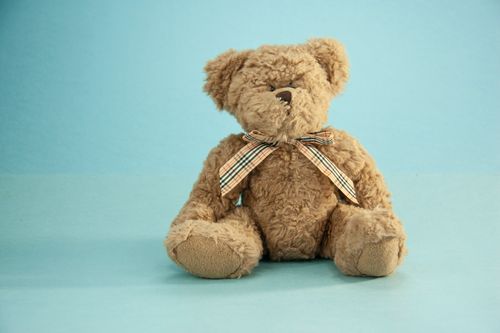 Free Cute fluffy brown colored teddy bear with funny bow sitting on blue background Stock Photo