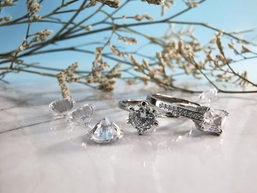 Free Elegant silver wedding rings with diamonds and crystals placed on shiny white table with twigs of tree on light blue background Stock Photo