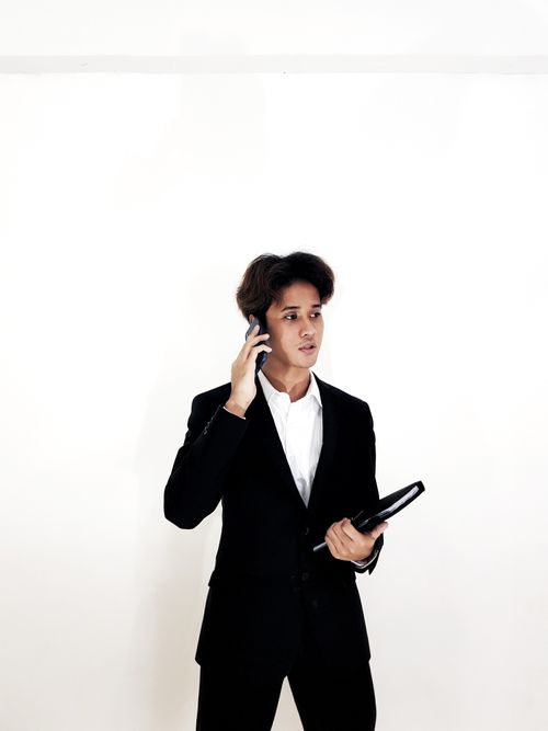 Free Professional businessman in black suit talking on smartphone, indoor setting. Stock Photo