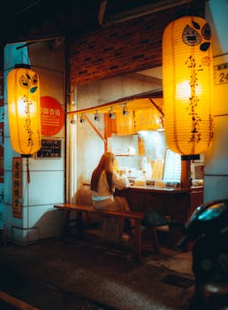 A woman enjoys a meal at an illuminated food stall at night.