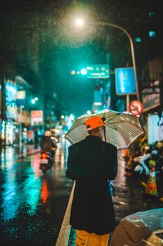 Person with umbrella on a rainy urban night street, showcasing vibrant city lights and reflection.