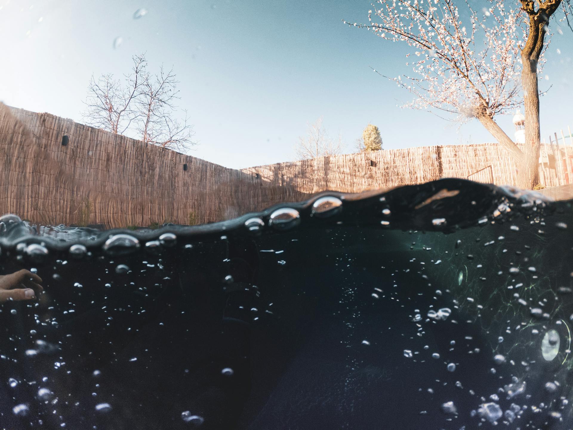 Captivating half-submerged view of a pool with splashing water bubbles under a clear sky.