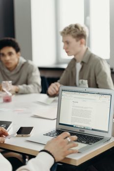 Group of young adults working together in a modern office setting, focusing on a laptop.