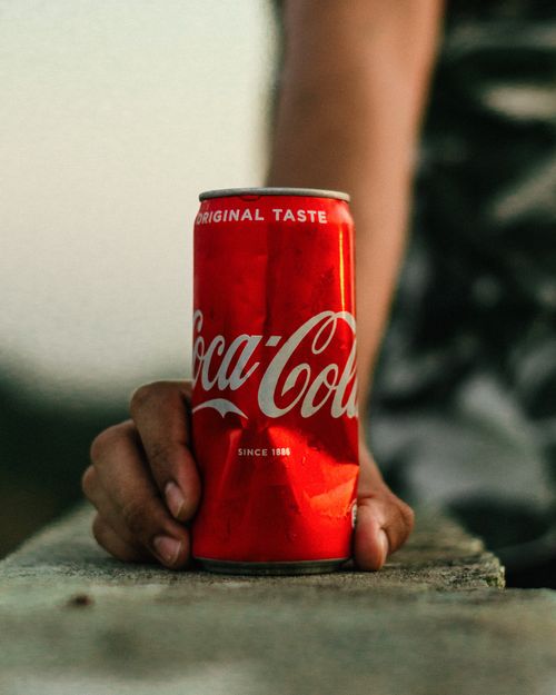 Free A close-up shot of a hand holding a Coca-Cola can outdoors on a bright day. Stock Photo