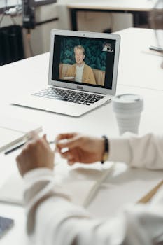 Professional virtual meeting with focus on laptop screen showing a video call participant.